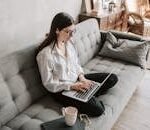 Woman in a cozy home setting working on a laptop for remote work and relaxation.