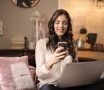 A woman enjoying leisure time using her smartphone and laptop in a cozy living room.